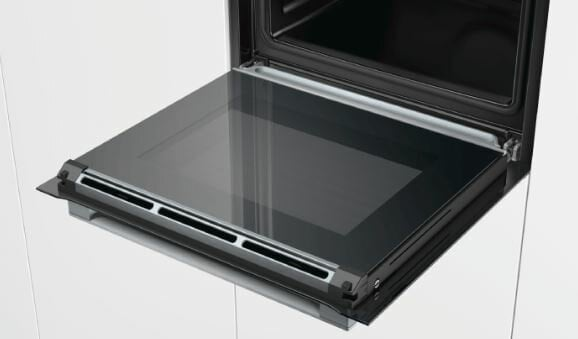 Otwarte drzwi piekarnika z szybą. Widoczne wnętrze piekarnika i białe szafki.