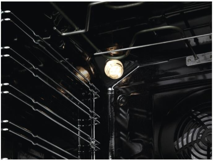 Wnętrze piekarnika. Światło jest włączone, widoczne są metalowe ruszty. Czarne wnętrze.