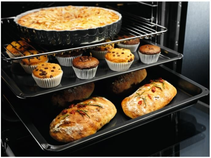 Wnętrze piekarnika z jedzeniem na półkach: zapiekanka w czarnym naczyniu, muffiny i chleb.