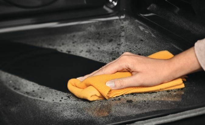 Ręka wyciera wnętrze ciemnego piekarnika pomarańczową szmatką, usuwając resztki.