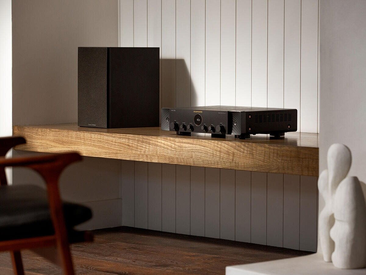 Czarny sprzęt audio na drewnianej półce na tle białej ściany.