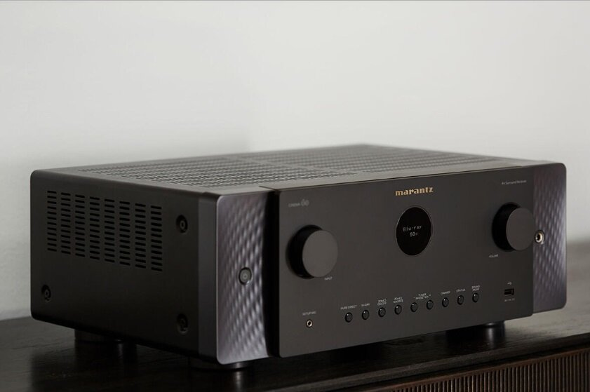 Czarny amplituner Marantz AV na ciemnej powierzchni. Widoczne przyciski i wyświetlacz.