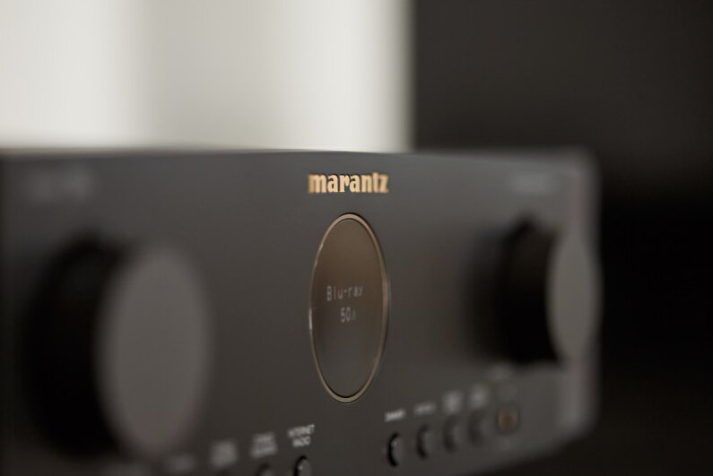Zbliżenie czarnego odbiornika audio Marantz. Widoczna nazwa marki, a także wyświetlacz i przyciski.