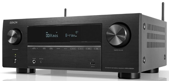 Czarny odbiornik Denon z wyświetlaczem i pokrętłami, anteny na górze. Białe tło.