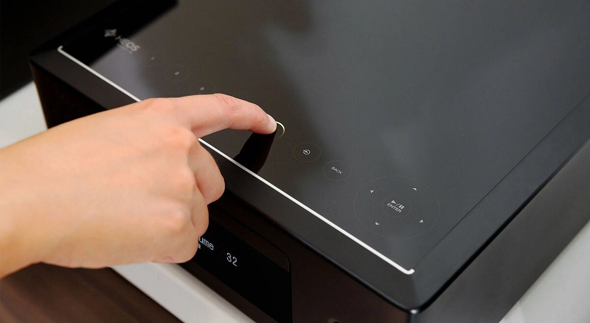 Palec naciska przycisk na czarnym urządzeniu HEDOS.