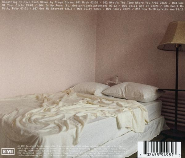 Bett mit weißer Bettwäsche, einer Lampe und einer Trackliste von Songs auf der Rückseite.