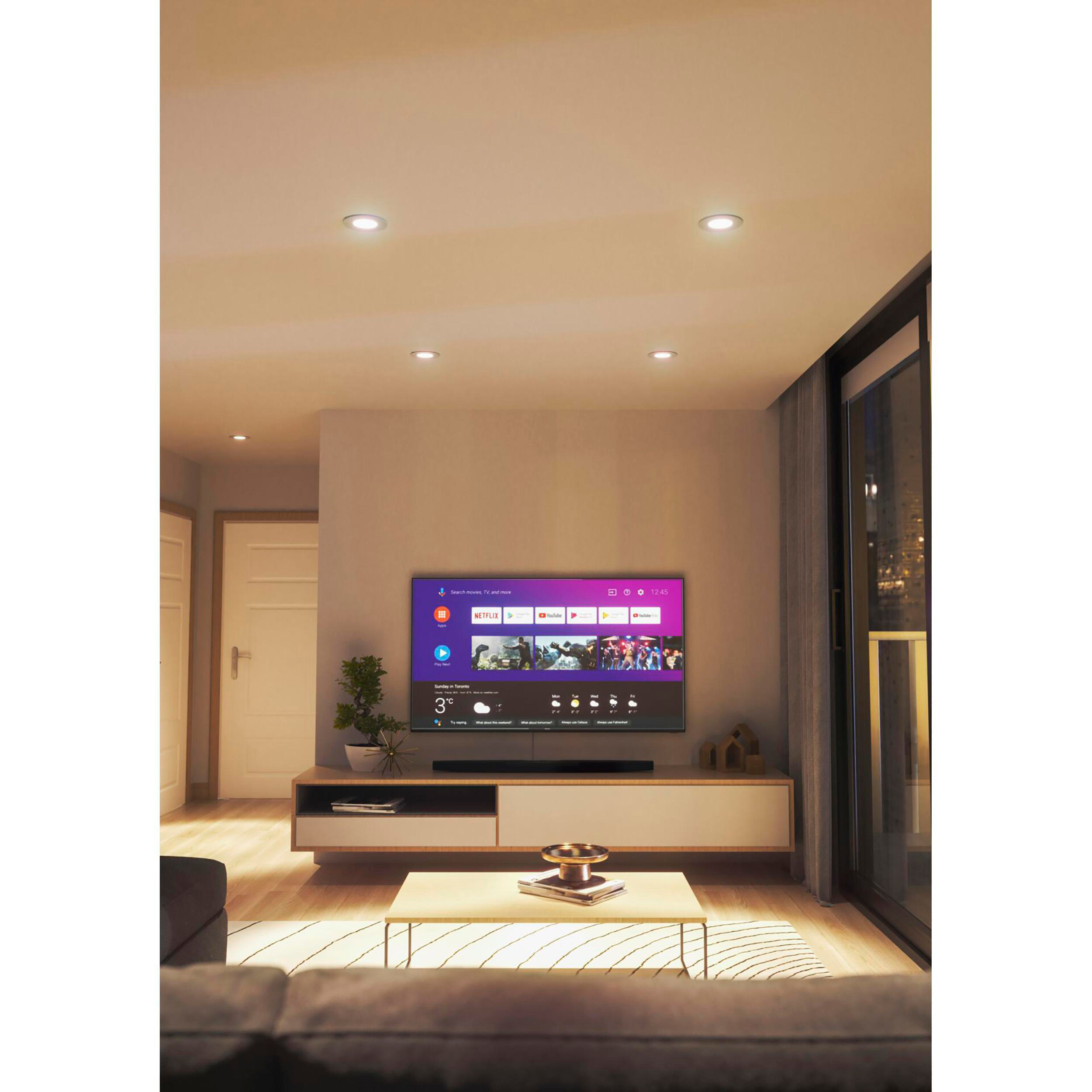 Ein modernes Wohnzimmer mit Fernseher auf einem Ständer. Einbaustrahler und Ecksofa vorhanden.