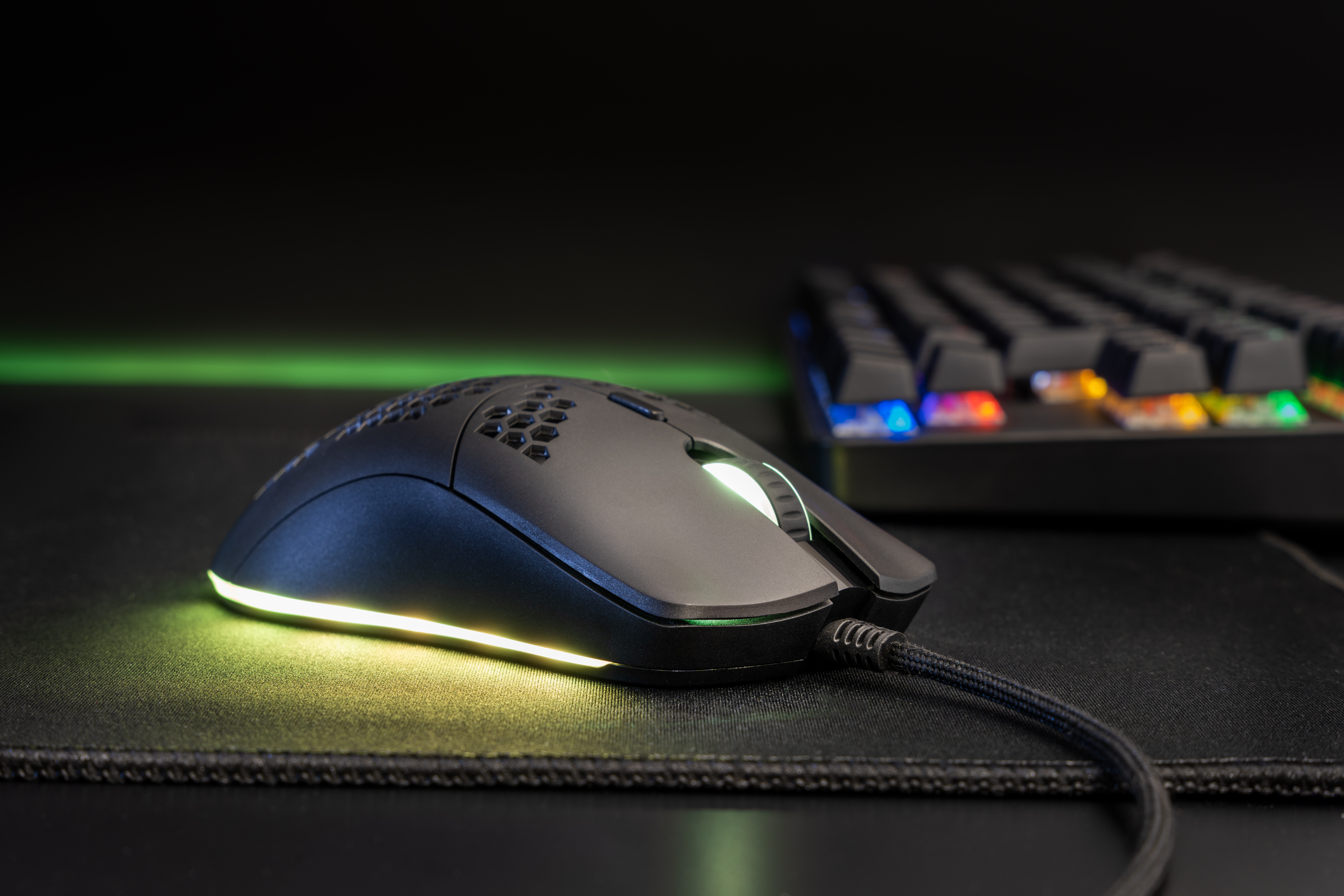 Souris de jeu noire avec éclairage RVB, à côté d'un clavier sur un tapis de souris de jeu. Fond sombre.