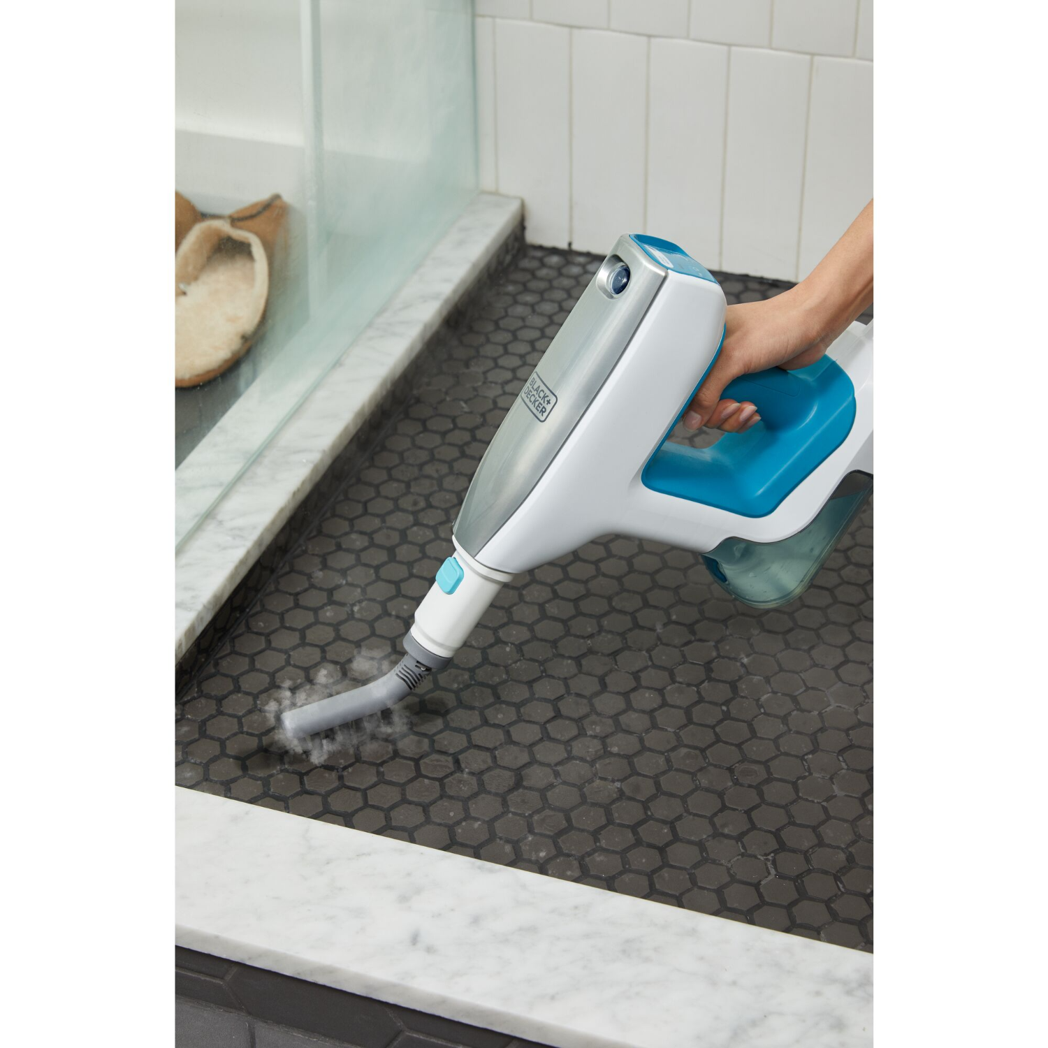 Person cleaning a black tiled shower floor with a white and blue steam cleaner.