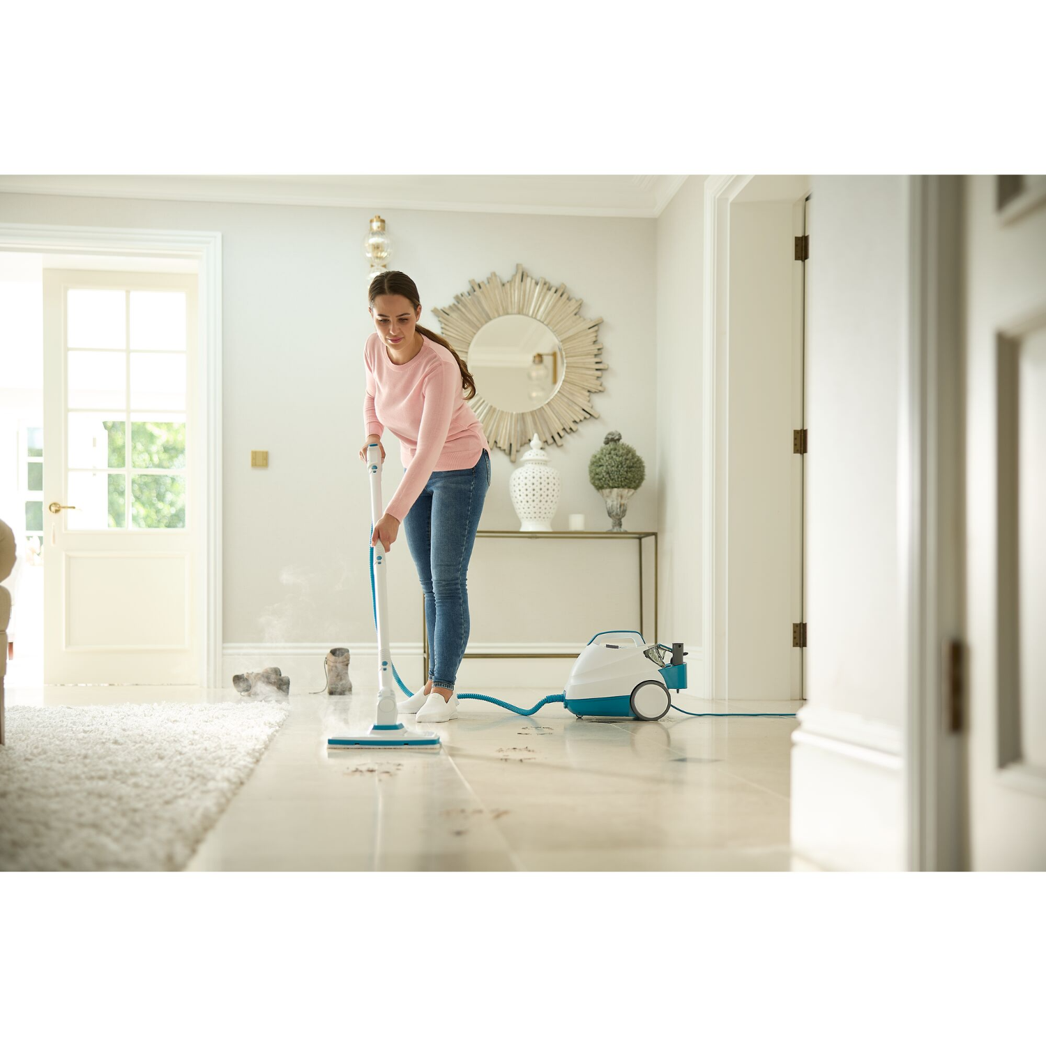 Woman cleaning a floor with a steam cleaner. A rug and scattered dirt are in the foreground.
