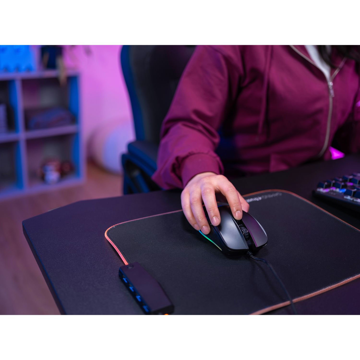A person's hand using a black gaming mouse on a mousepad. The mousepad has RGB lighting.