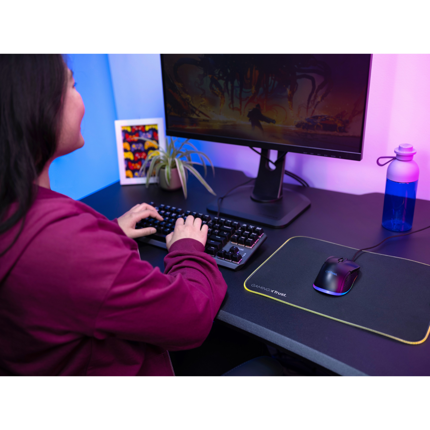 A woman using a keyboard and mouse at a desk with a monitor and a water bottle.