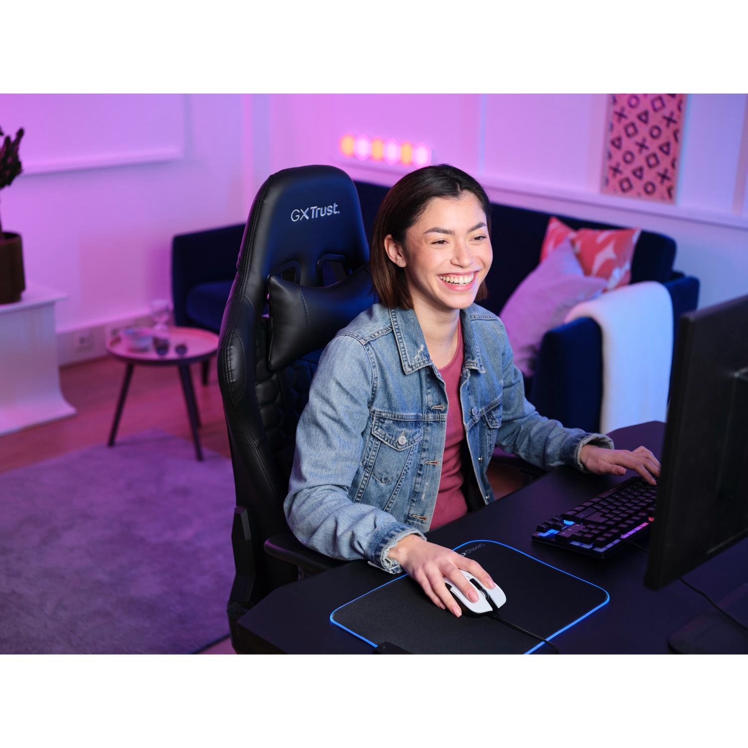 Woman smiling while using a computer, with a gaming setup.