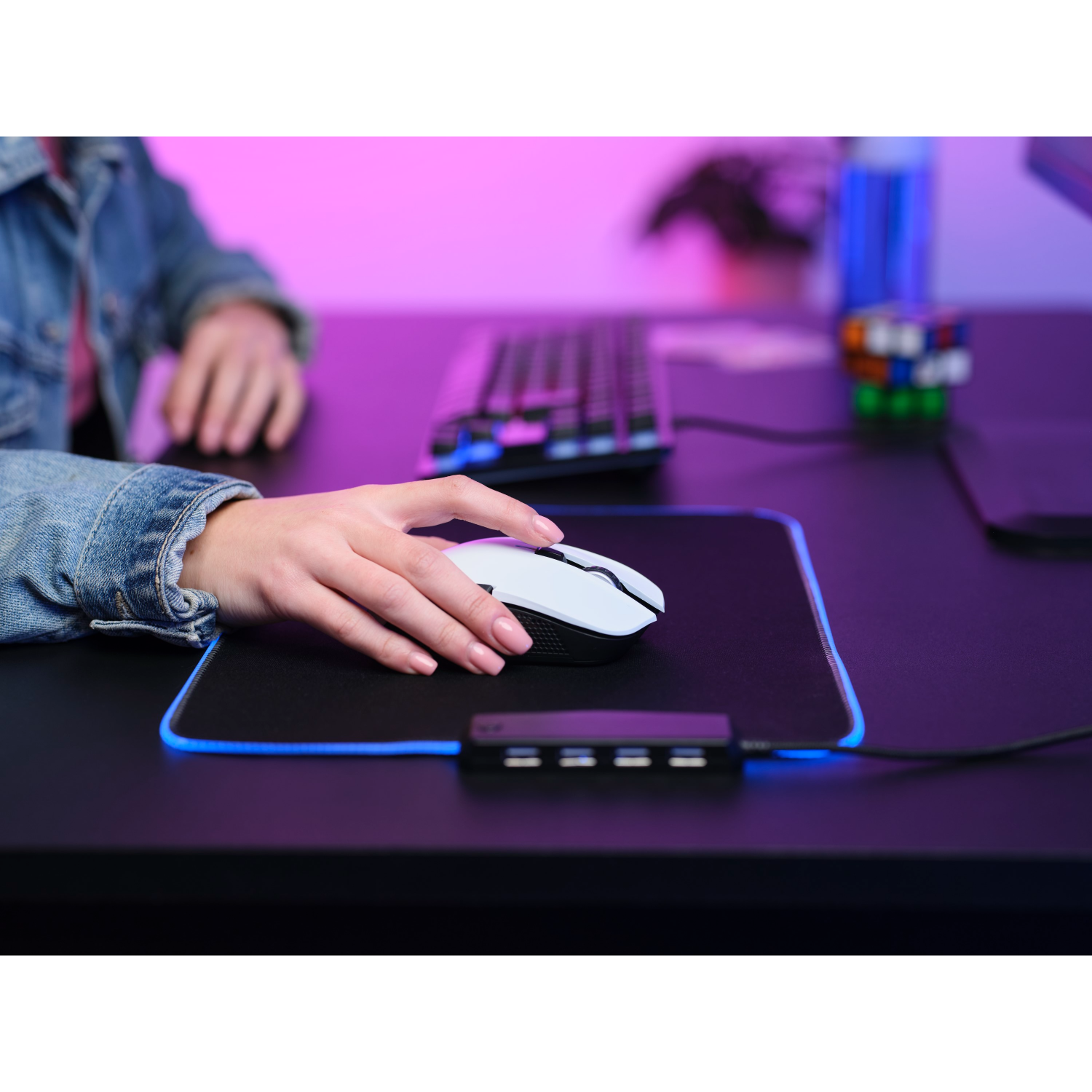 Person using a white mouse on a black mousepad with a keyboard and cube in the background.