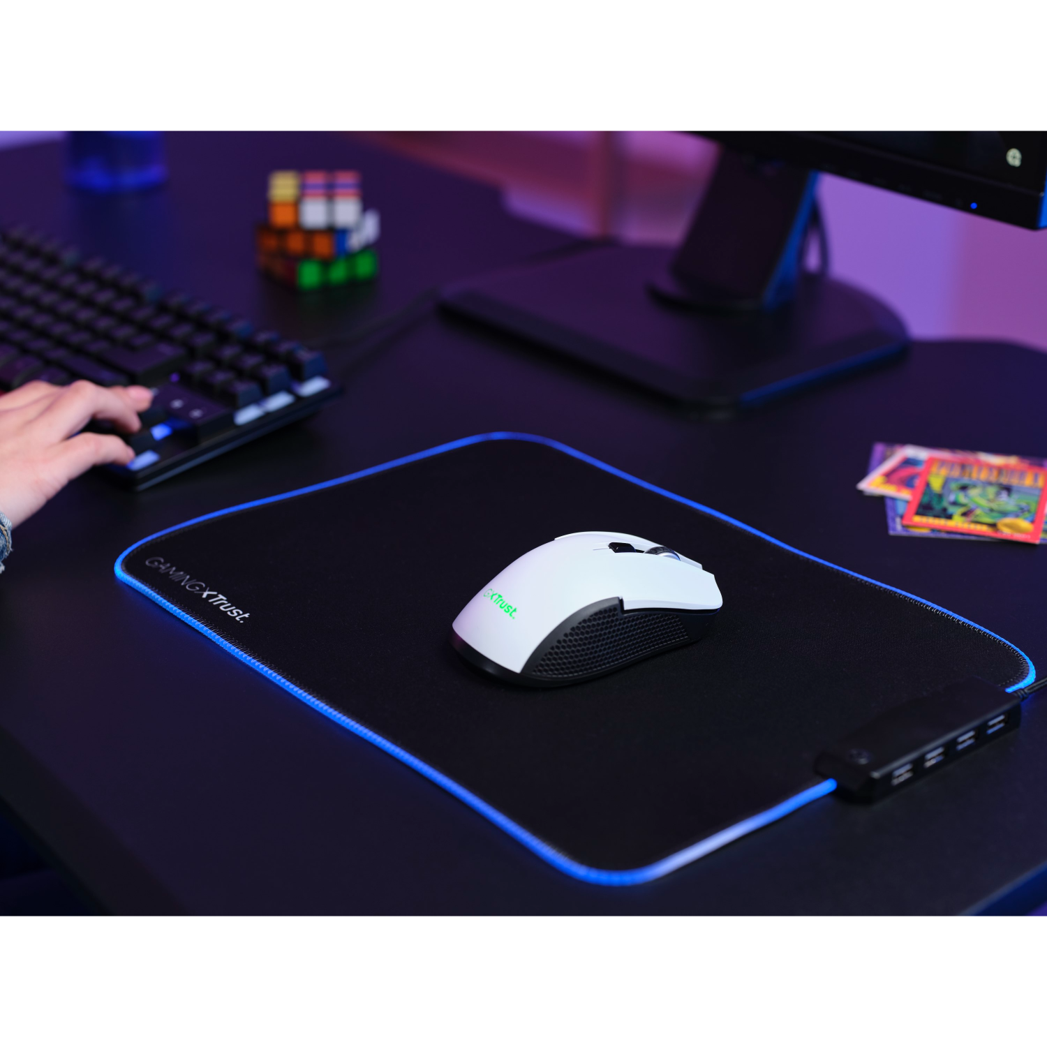 A gaming setup with a white mouse on a black mousepad with blue edges, and a keyboard.