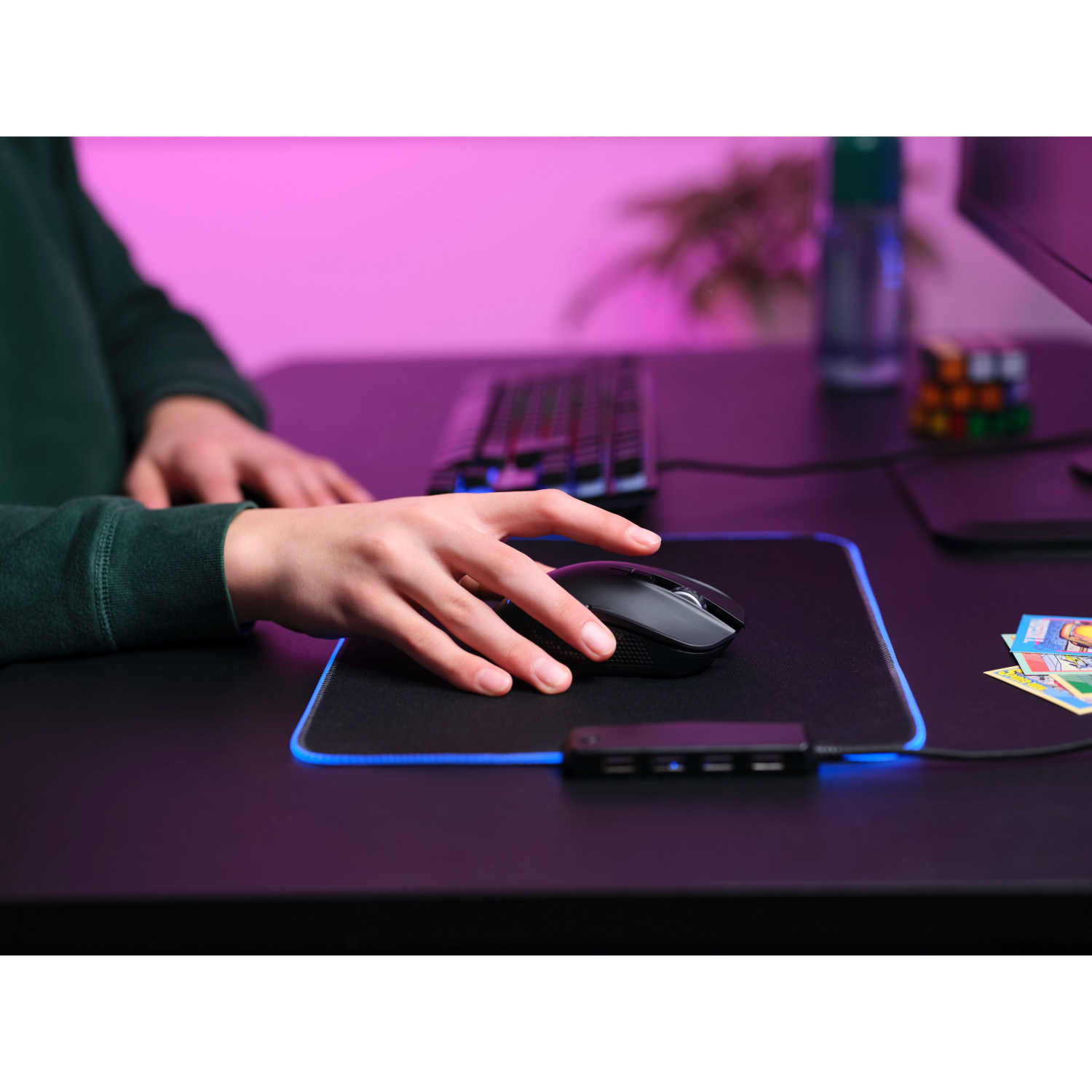 A person using a black mouse on a gaming mousepad with a keyboard and cards on a desk.
