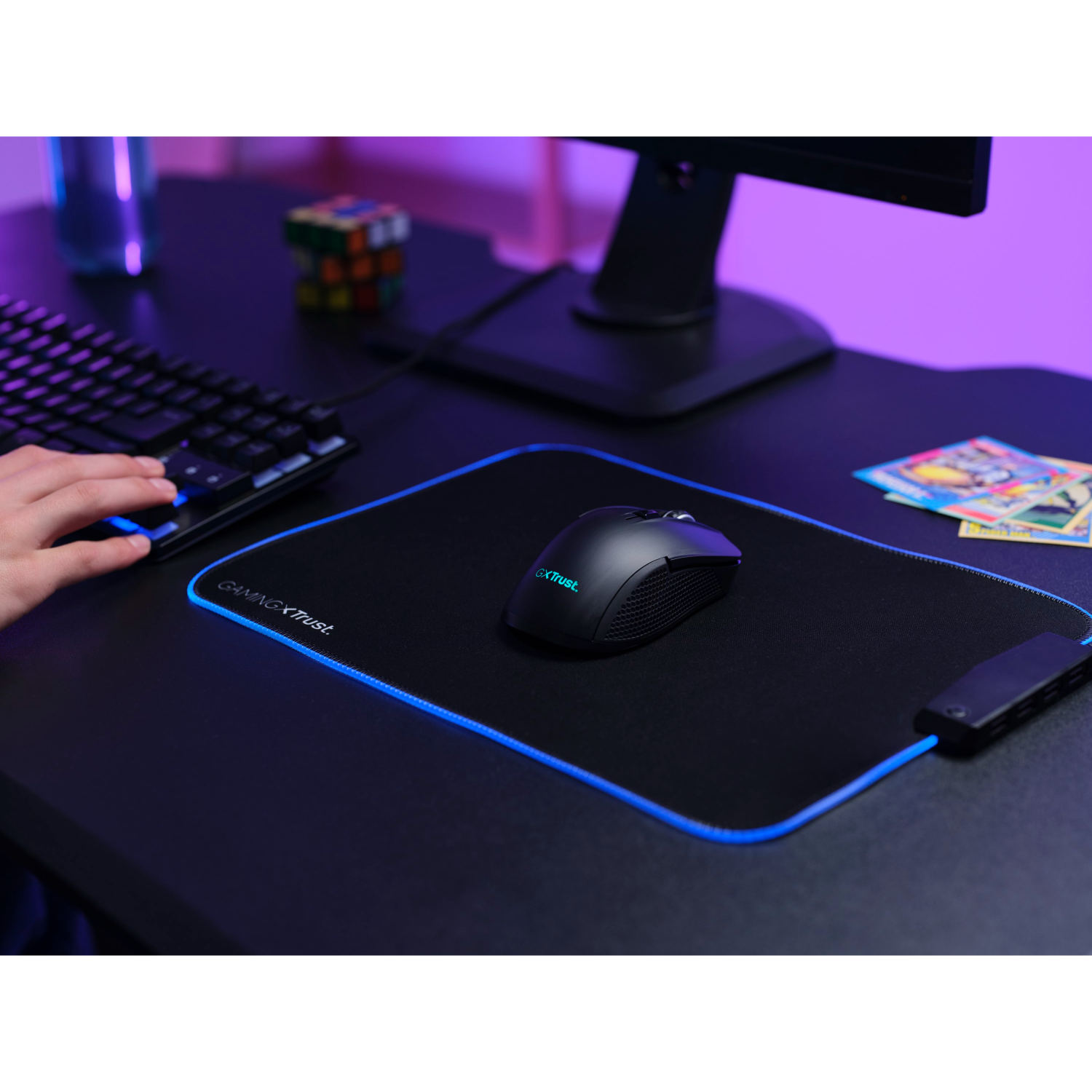 Gaming setup: Black mouse on a black mousepad with blue accents, keyboard, monitor, and cards.