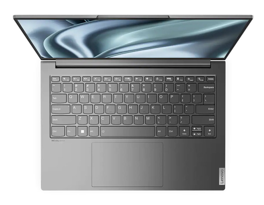 Laptop, widok z góry, otwarty. Srebrna obudowa, widoczna klawiatura i tło z falistym wzorem.