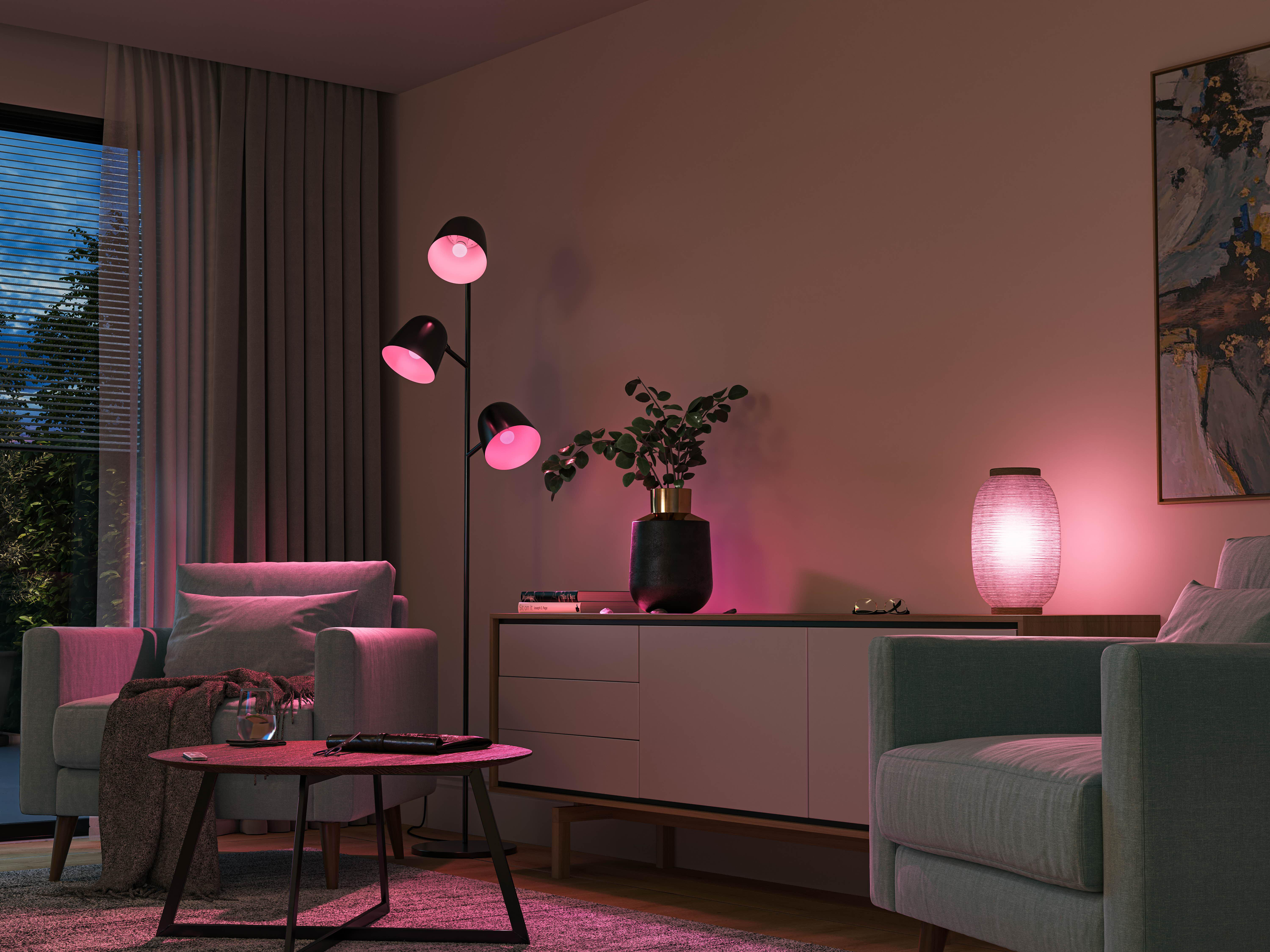 Wohnzimmerszene mit Steh- und Tischleuchte, beide strahlen rosa Licht aus.