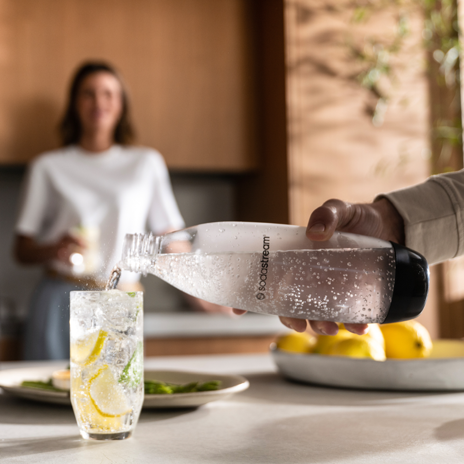 Een persoon giet water uit een SodaStream-fles in een glas met ijs en citroen.