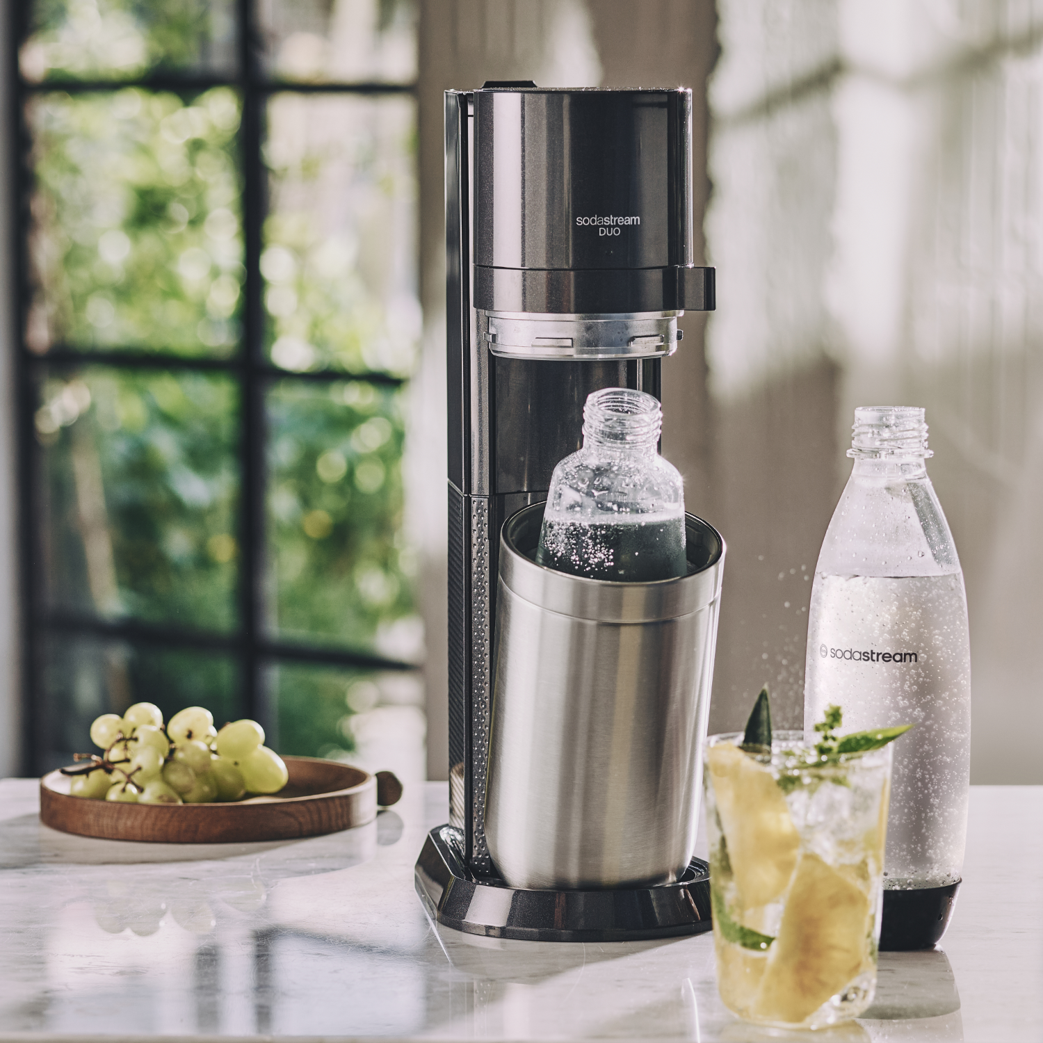 SodaStream Duo-machine met een fles erin, een cocktail, druiven en een sodafles.