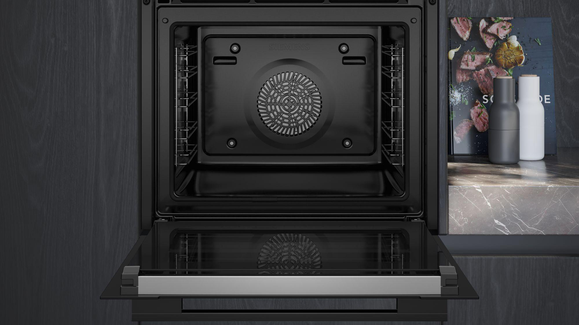 Backofen-Innenraum mit offener Tür. Der schwarze Innenraum hat Gitter, einen Ventilator und ein Licht. Dunkler Holzuntergrund.