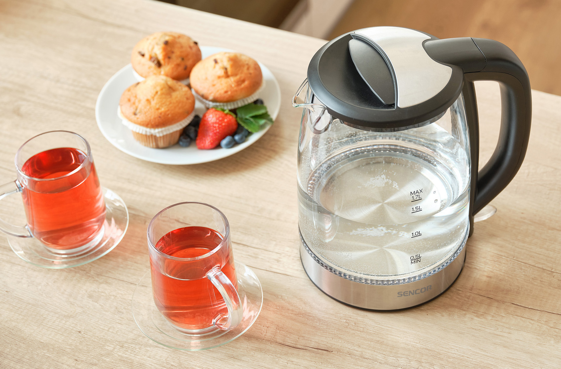 Tea és muffinok az asztalon. Egy üveg elektromos vízforraló van az asztalon vízzel.