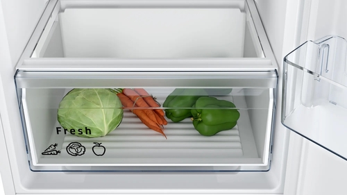Cajón del refrigerador lleno de repollo, zanahorias y pimientos verdes.