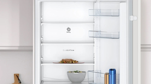 Interior de un refrigerador blanco abierto, mostrando estantes, comida y la función EcoAirFlow.