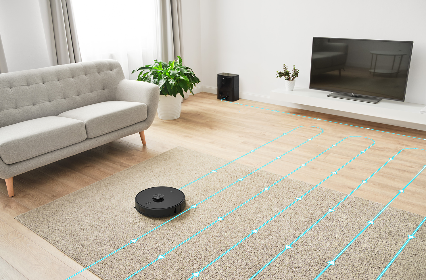 Egy fekete robot porszívó egy világosbarna szőnyegen. A szőnyeg egy kanapéval és TV-vel rendelkező szobában van.