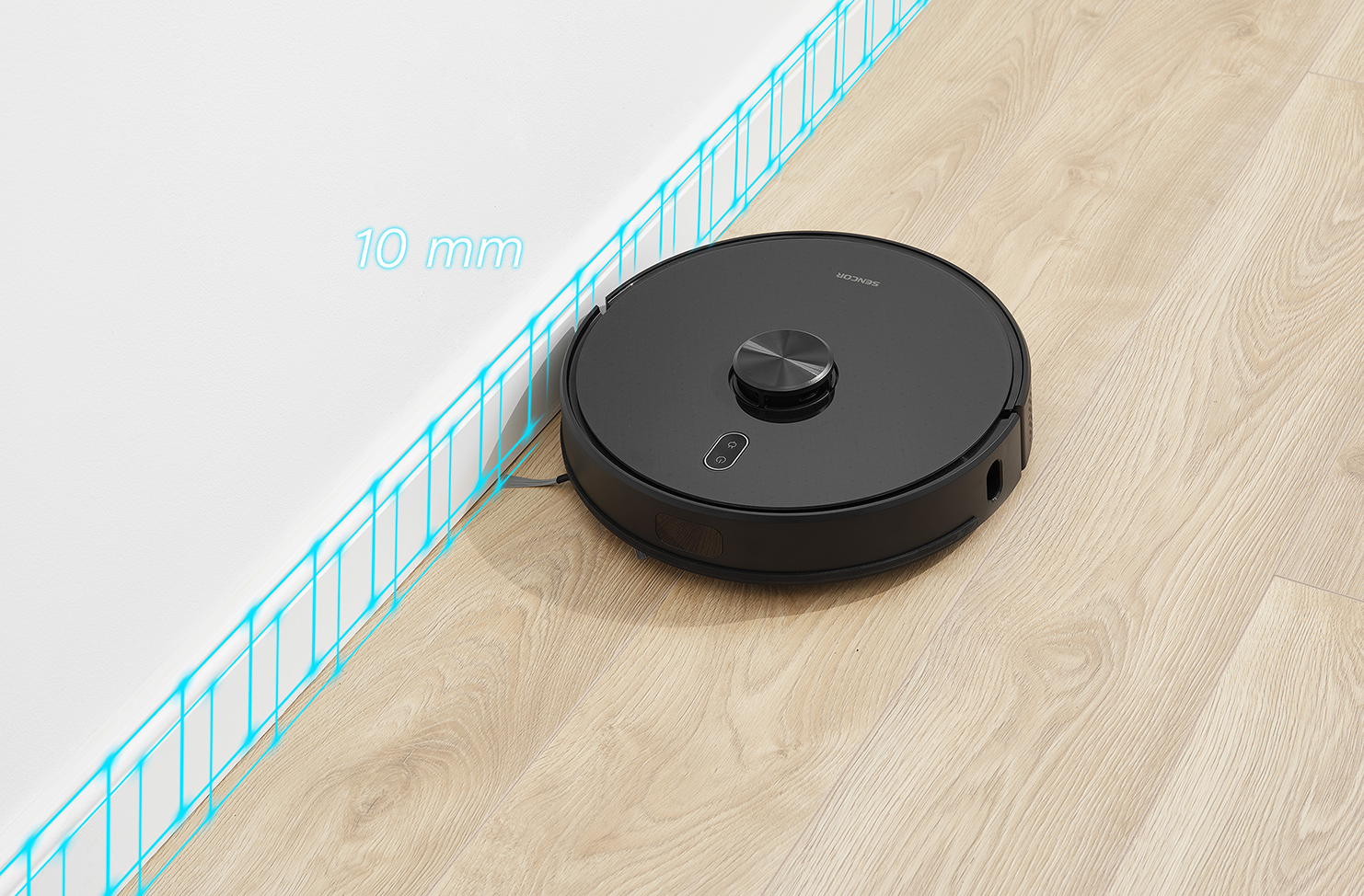 Fekete robotporszívó egy fehér fal közelében, fa padlón.