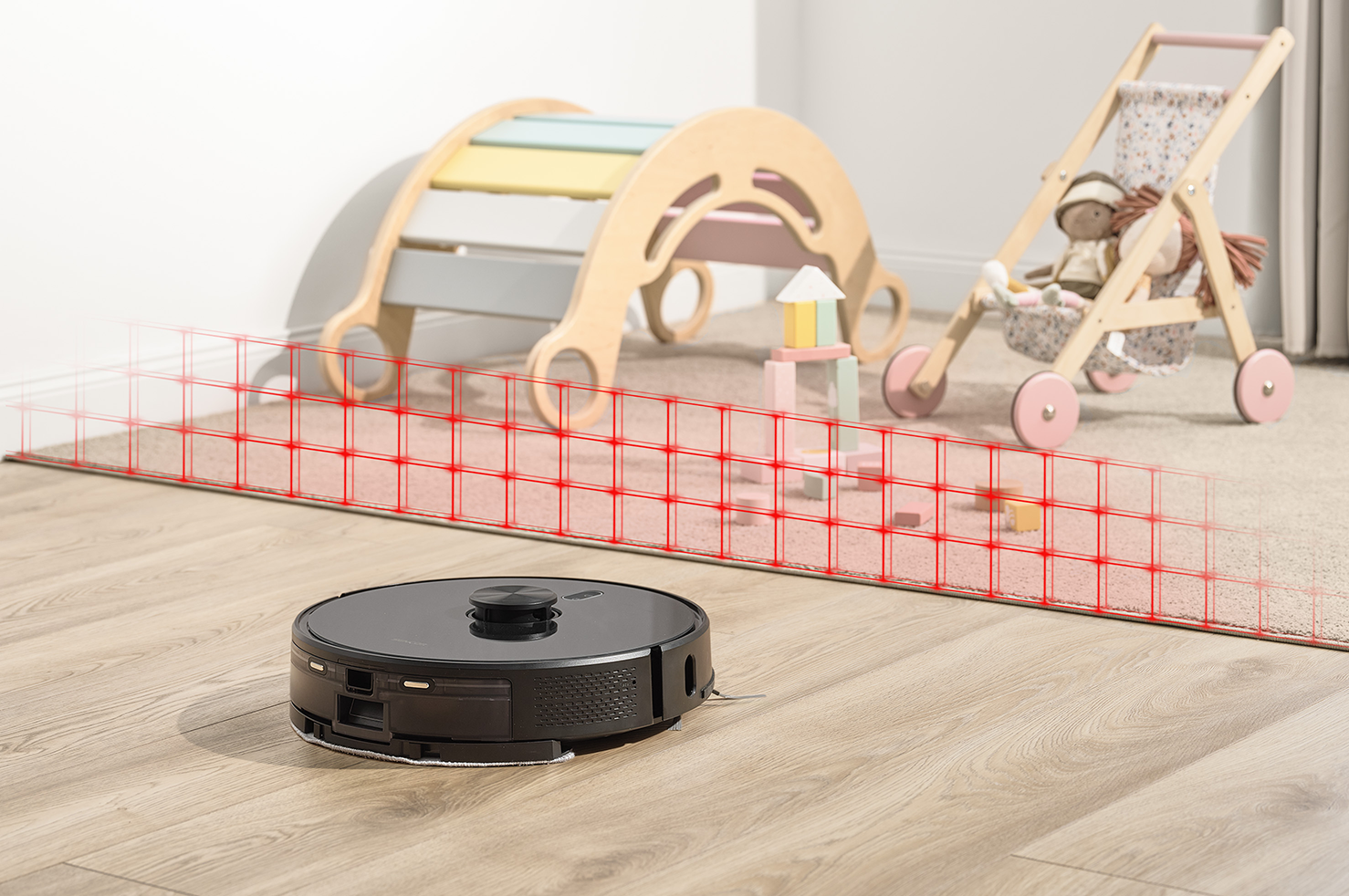 Robotporszívó egy fa padlón. A háttérben egy rózsaszín szőnyeg és játékok vannak.