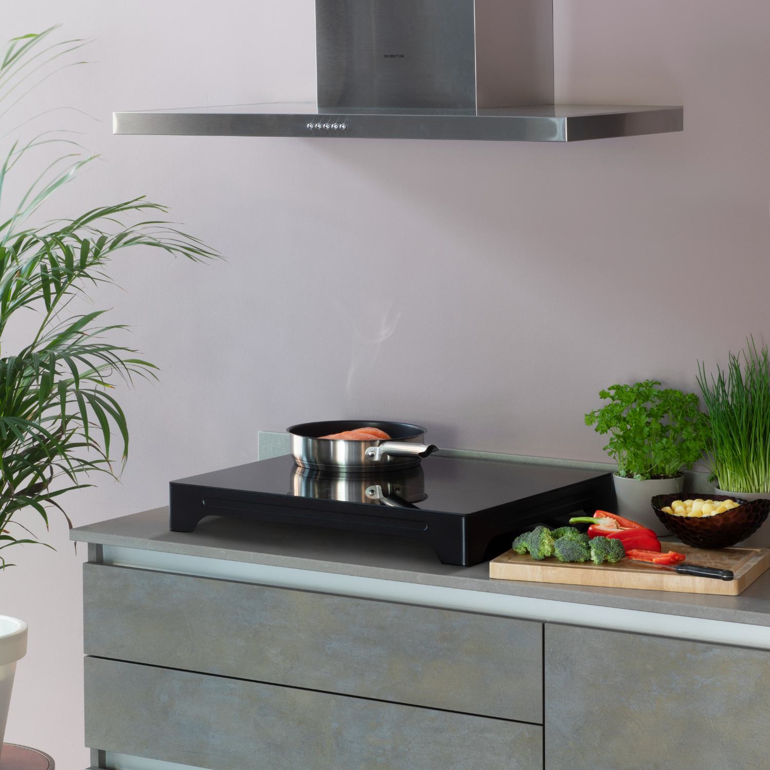 Kitchen scene with a cooking surface and ingredients. A pan with food is on the surface, near veggies.