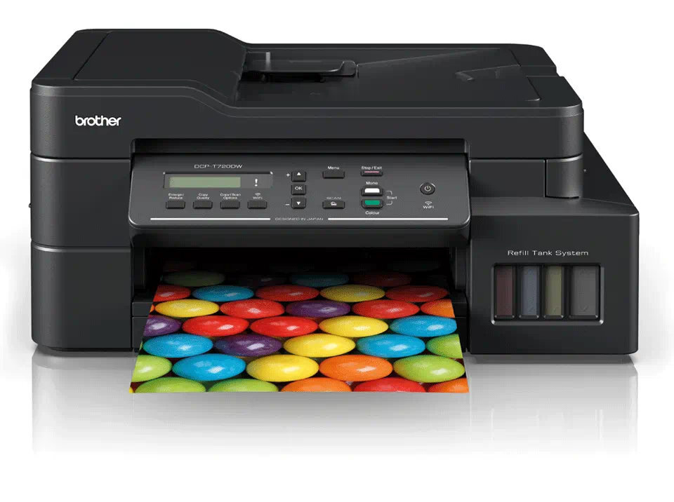 Czarna drukarka Brother drukująca kolorowy obraz cukierków. Widoczny system napełniania zbiornika.