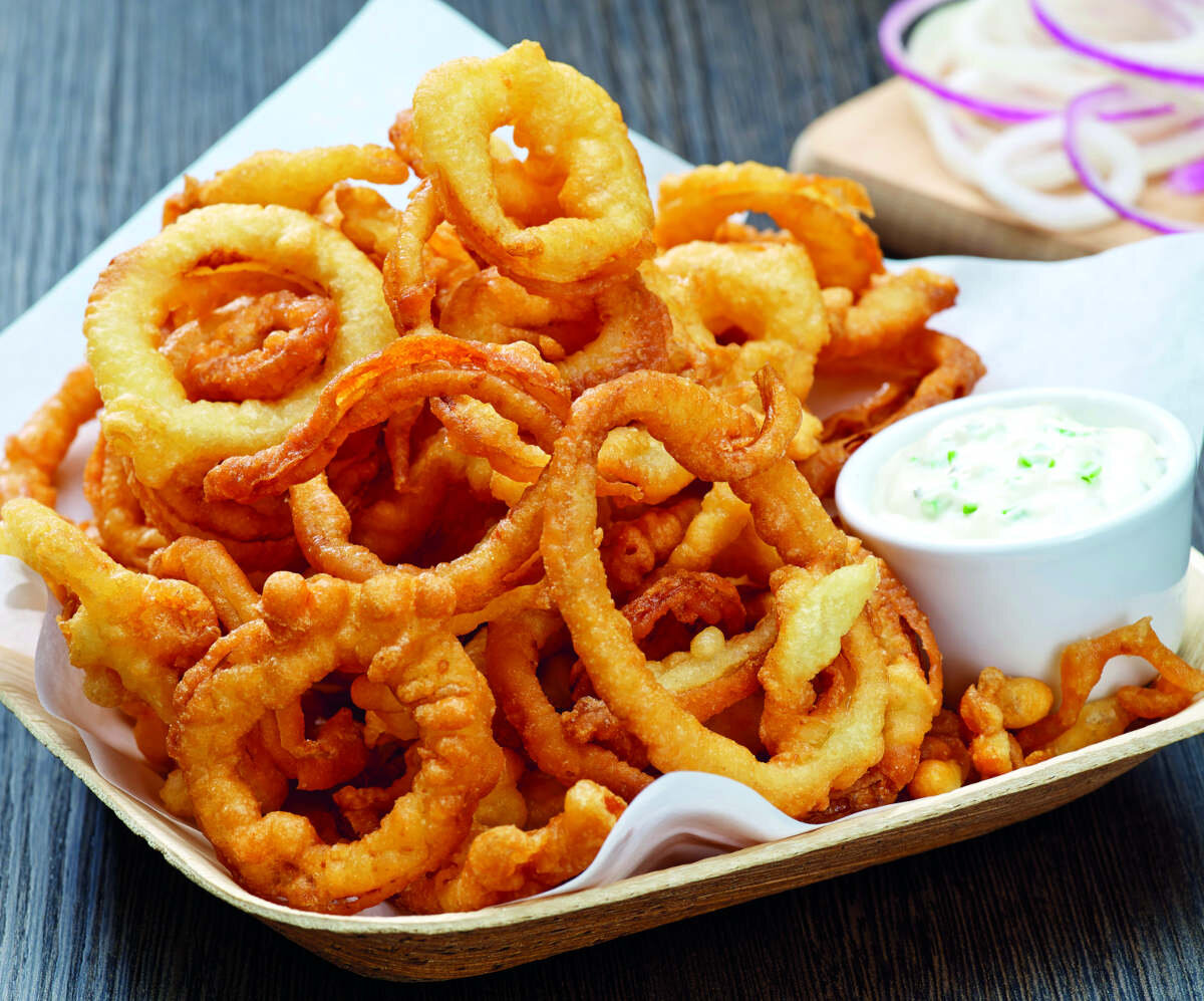 Chrupiące smażone krążki cebulowe podane na drewnianej tacy z białym sosem.