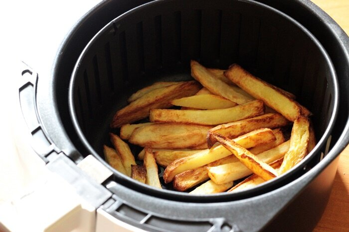 Kosz do frytkownicy powietrznej wypełniony złocistobrązowymi, ugotowanymi frytkami, zbliżenie.