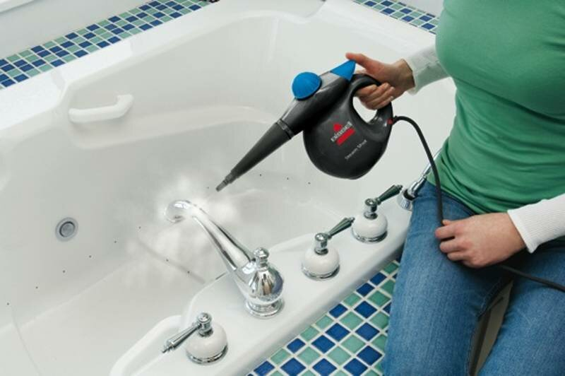 Osoba czyszcząca białą wannę za pomocą parownicy ręcznej.