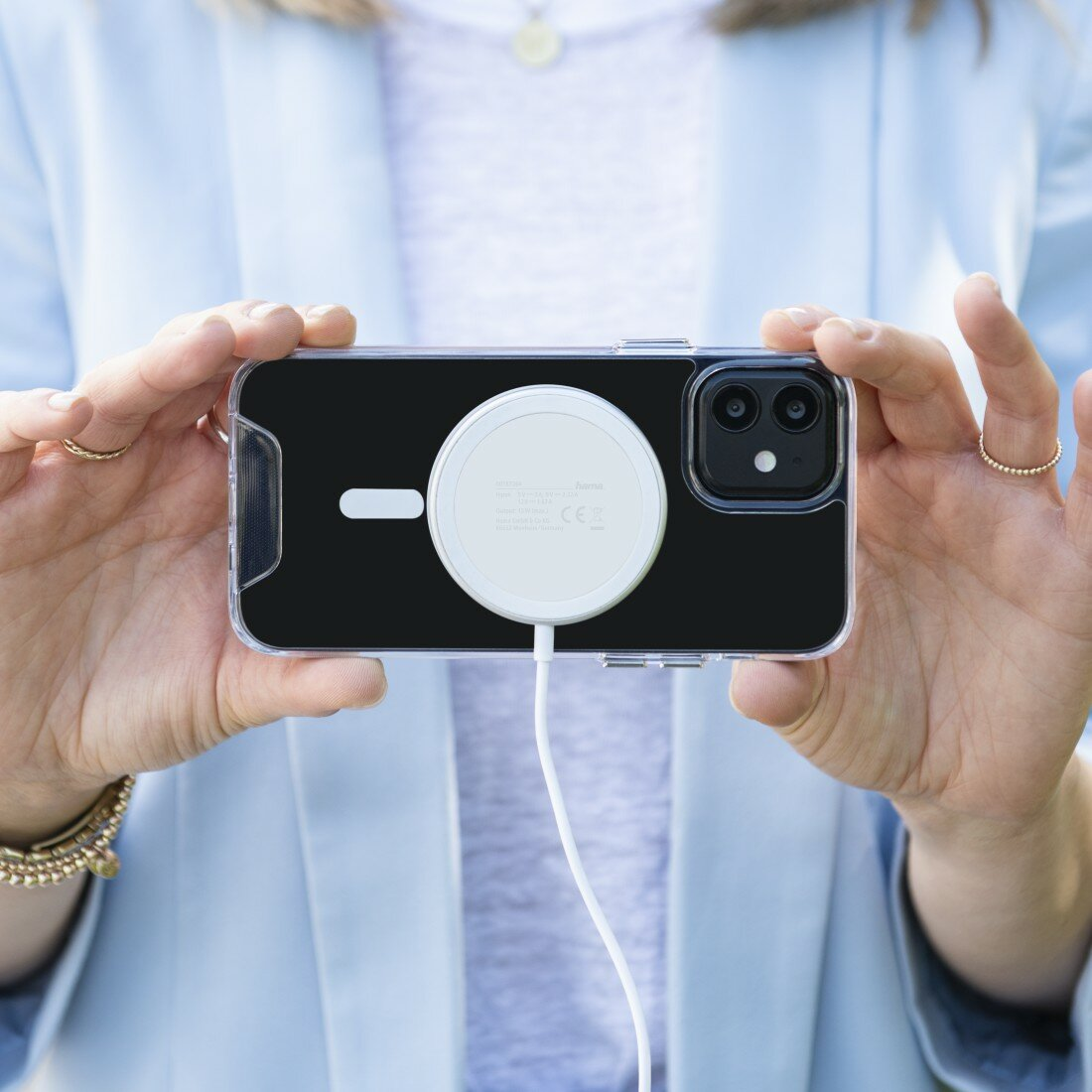 Osoba trzymająca iPhone z ładowarką MagSafe. Przezroczyste etui.