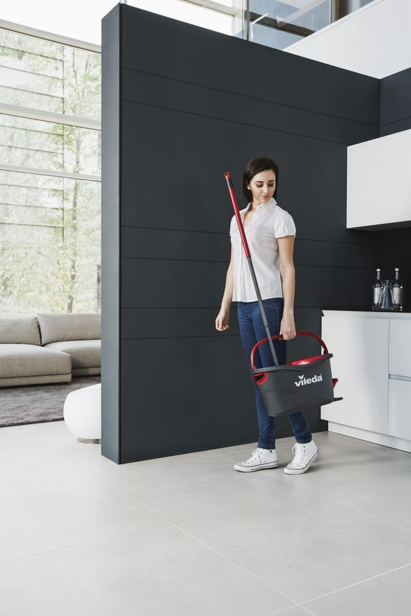 Kobieta w białej koszuli i dżinsach niesie mop i wiadro w nowoczesnej, czystej kuchni.