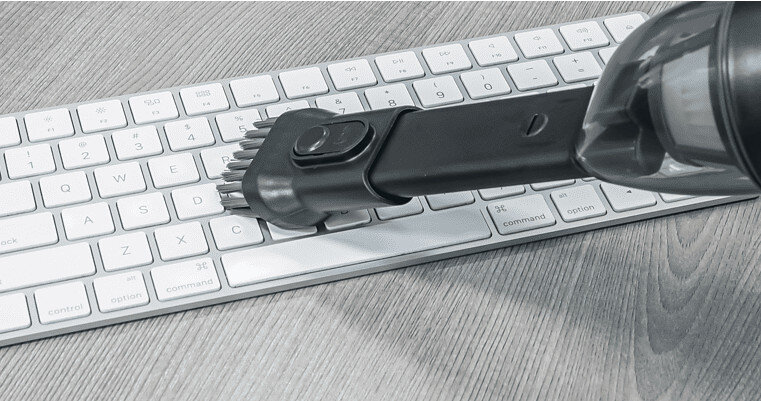 Odkurzacz czyszczący białą klawiaturę na drewnianej powierzchni.