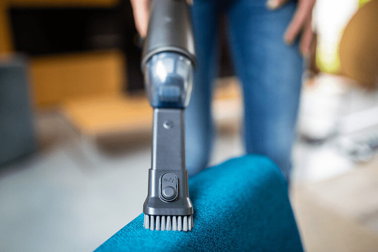 Głowica odkurzacza czyszcząca niebieski fotel. Szczotka dotyka tkaniny.