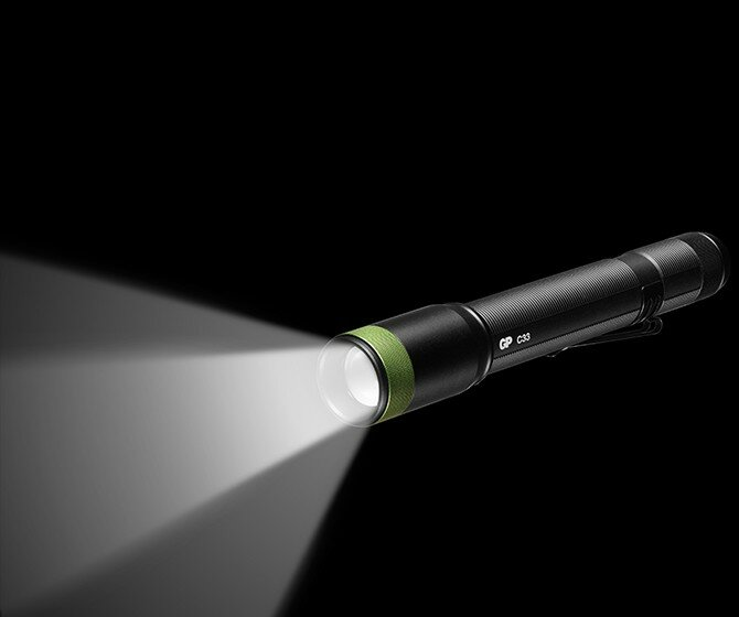 Czarna latarka z zielonym pierścieniem, emitująca wiązkę światła na czarnym tle.