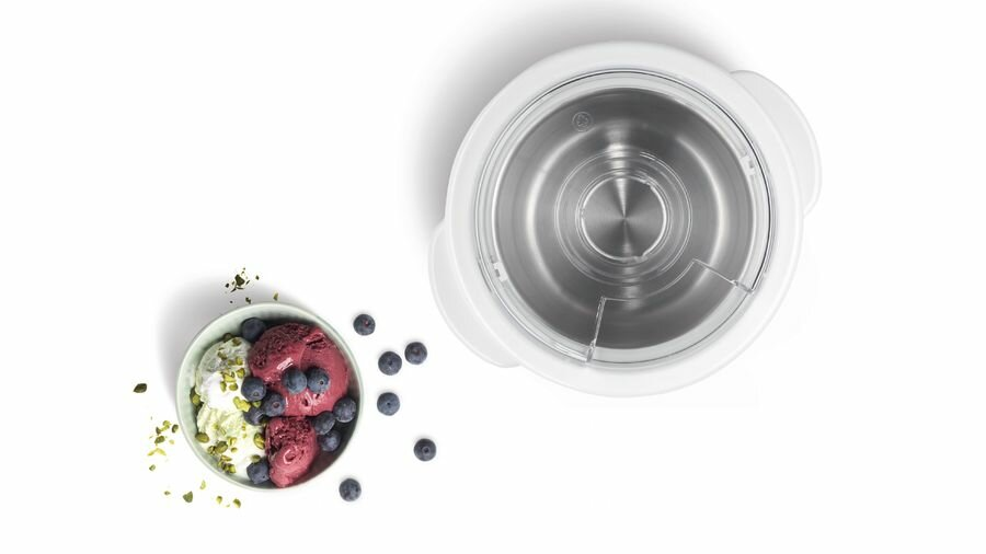 Lody w misce z jagodami i biała maszyną do lodów.