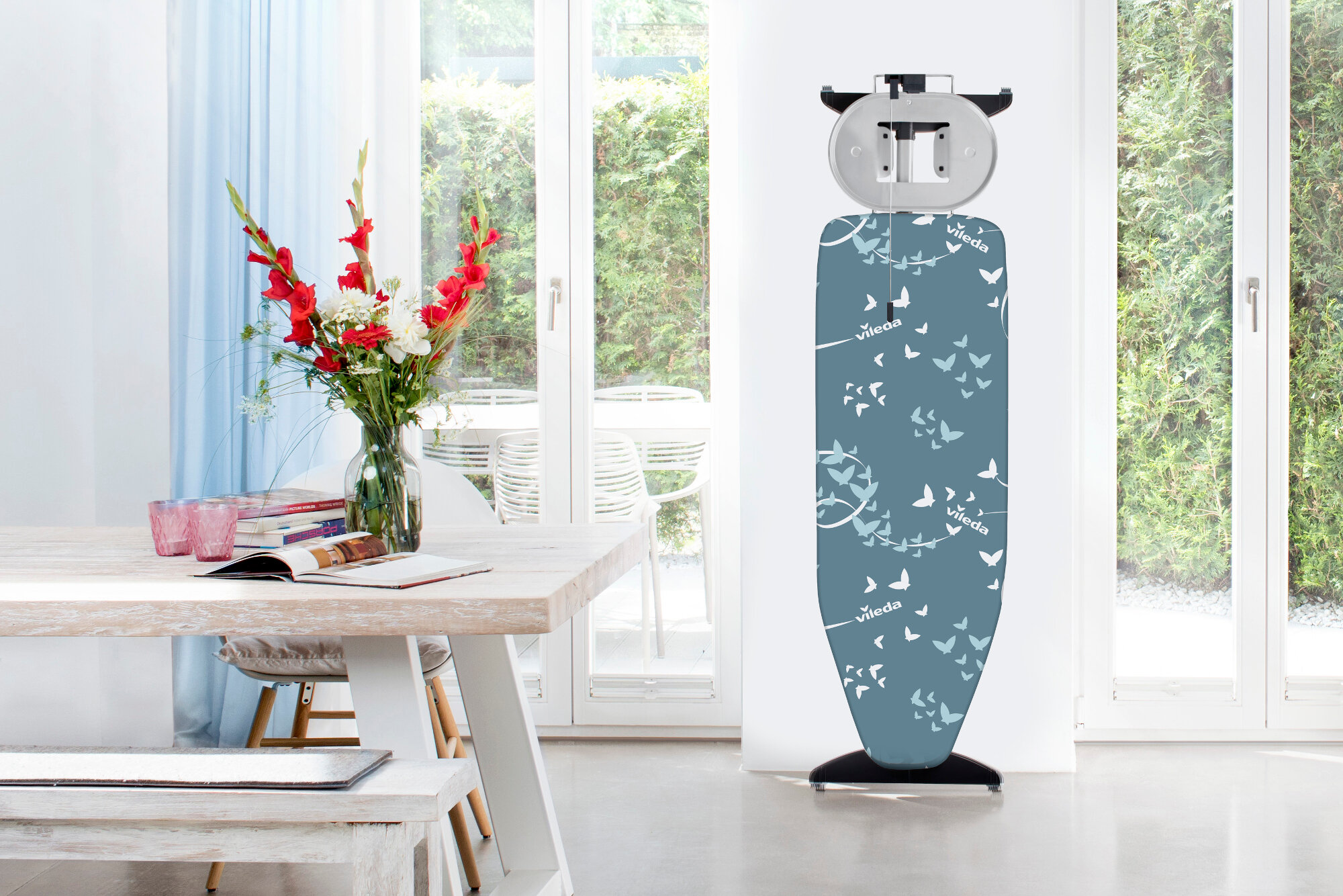 Deska do prasowania z motywem motyli. W pobliżu wazon z kwiatami.