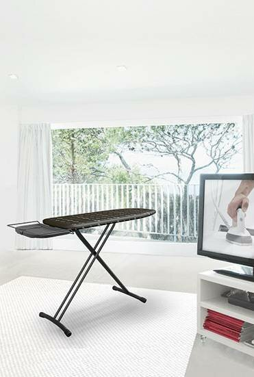 Otwarta deska do prasowania w jasnym pokoju z dużym oknem z drzewami i telewizorem.