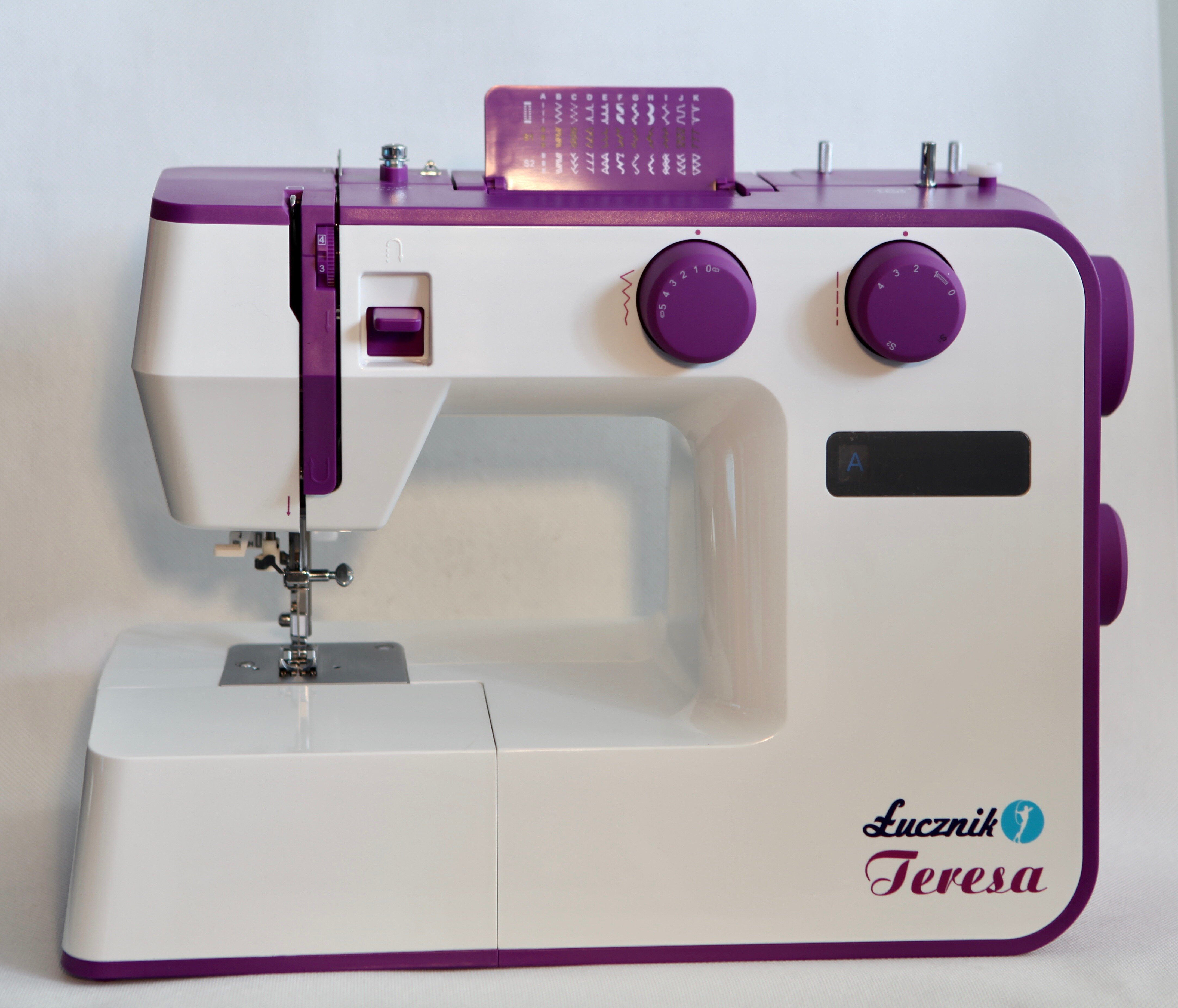 Biało-fioletowa maszyna do szycia. Ma dwa pokrętła, igłę i nazwę 'Lucznik Teresa'.