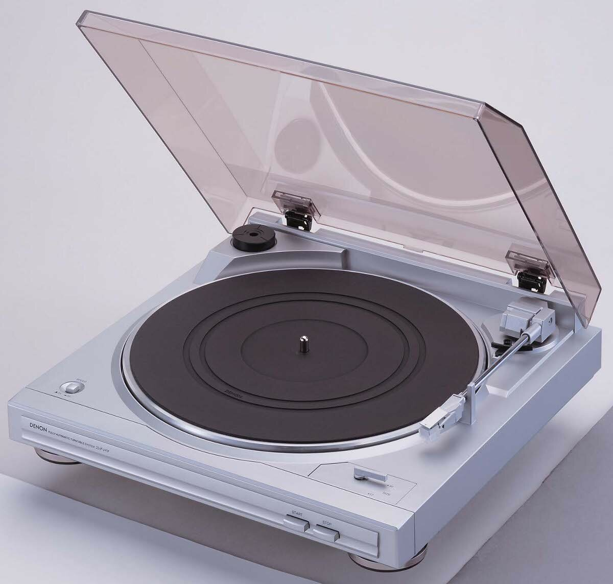 Srebrny gramofon z otwartą pokrywą. Czarna płyta na talerzu. Gramofon jest ustawiony pod kątem. Biała powierzchnia.