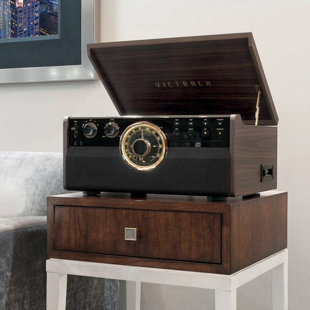 Drewniany gramofon Victrola z otwartą pokrywą na drewnianym stojaku, z ciemną szafką w tle.