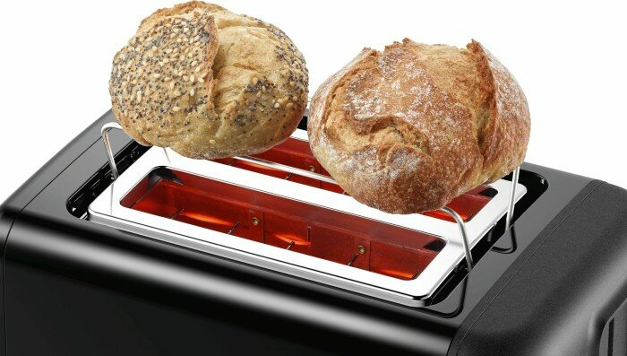 Czarny toster z dwoma okrągłymi bułkami na wierzchu. Wewnątrz widać czerwone światło od elementów grzejnych.