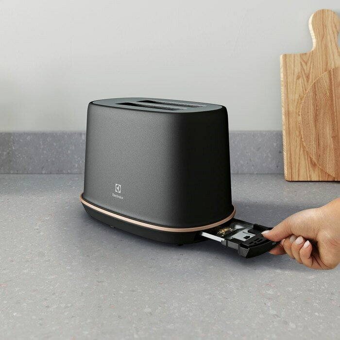 Czarny toster z wysuwaną tacą przez rękę. Toster stoi na szarym blacie.